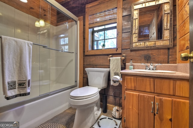 full bathroom featuring tile patterned floors, toilet, shower / bath combination with glass door, wooden walls, and vanity