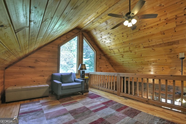 living area with light wood-style flooring, a ceiling fan, vaulted ceiling, wooden ceiling, and wood walls