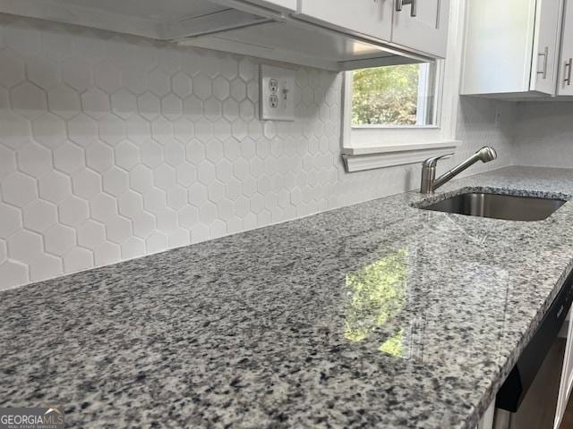 kitchen with backsplash, light stone countertops, white cabinetry, and a sink