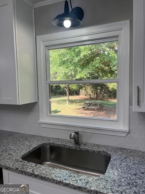 room details with light stone counters, white cabinets, backsplash, and a sink