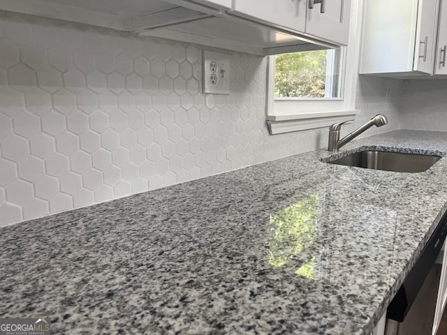 kitchen with white cabinetry, light stone counters, and sink