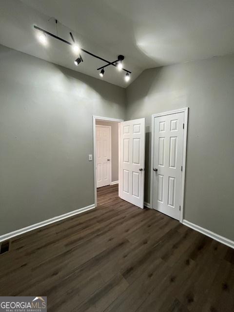 empty room featuring dark wood-style floors, track lighting, baseboards, and lofted ceiling