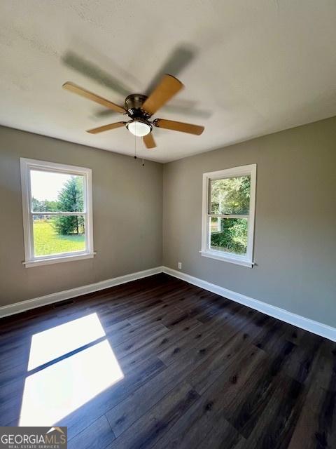 empty room featuring dark wood finished floors, baseboards, a wealth of natural light, and a ceiling fan