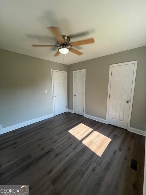 unfurnished bedroom featuring baseboards, dark wood-style floors, and a ceiling fan