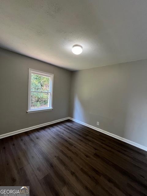 unfurnished room featuring baseboards and dark wood-style floors