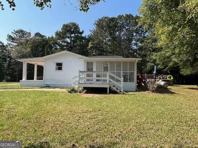 back of property featuring a wooden deck, a yard, and a sunroom