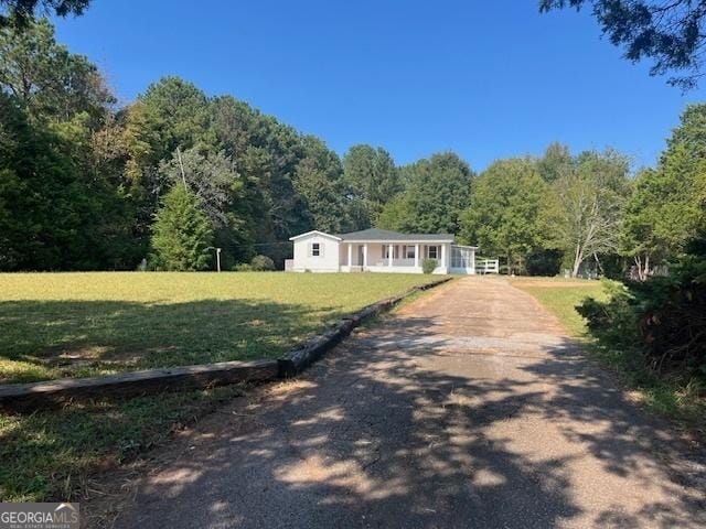 view of front facade with a front yard, a wooded view, and dirt driveway