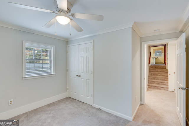 unfurnished bedroom featuring ornamental molding, a closet, light carpet, and ceiling fan