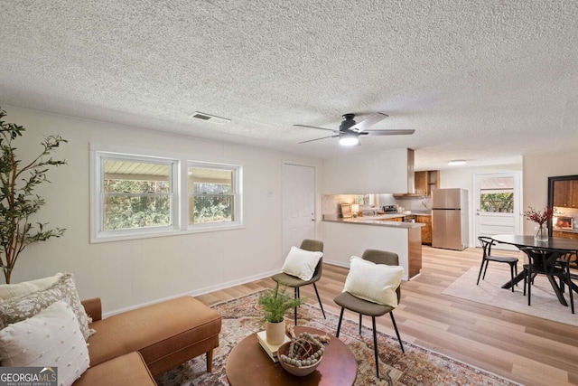 living room with a textured ceiling, light wood-type flooring, and ceiling fan