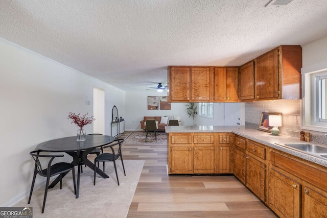 kitchen featuring tasteful backsplash, kitchen peninsula, light hardwood / wood-style flooring, and a textured ceiling