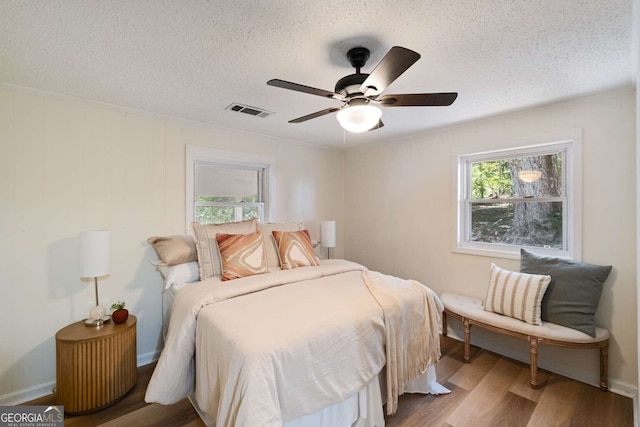 bedroom featuring hardwood / wood-style floors, ceiling fan, ornamental molding, and a textured ceiling