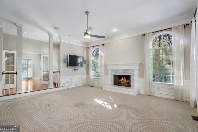 unfurnished living room with ceiling fan, a high end fireplace, ornamental molding, ornate columns, and light colored carpet