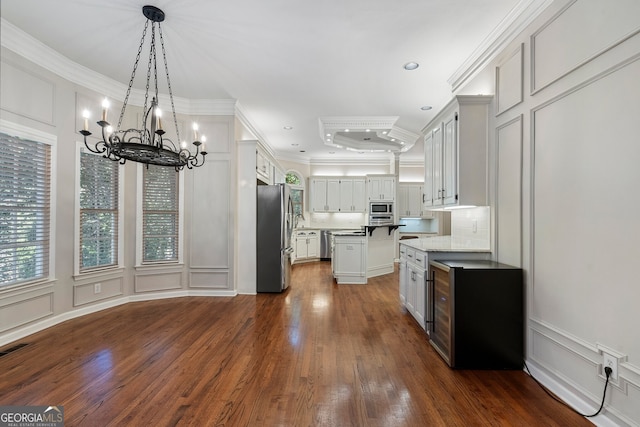 kitchen with appliances with stainless steel finishes, dark hardwood / wood-style flooring, white cabinetry, decorative light fixtures, and ornamental molding