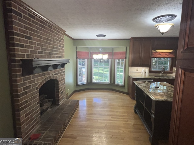 kitchen featuring light stone countertops, light wood-type flooring, a brick fireplace, a notable chandelier, and ornamental molding