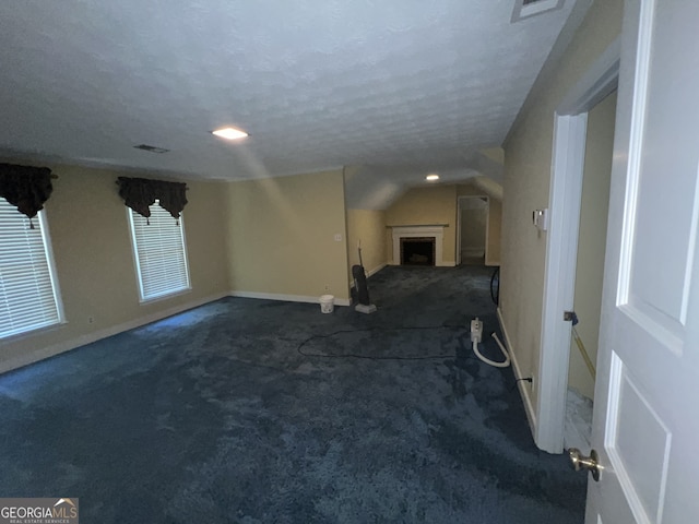 spare room with lofted ceiling, dark colored carpet, and a textured ceiling