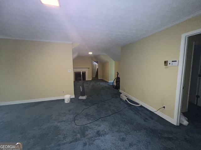 hall with ornamental molding, vaulted ceiling, dark colored carpet, and a textured ceiling