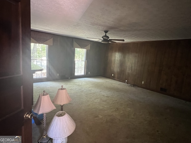 empty room featuring carpet, a textured ceiling, wooden walls, and ceiling fan