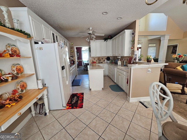 kitchen with kitchen peninsula, light tile patterned floors, white fridge with ice dispenser, ceiling fan, and white cabinetry