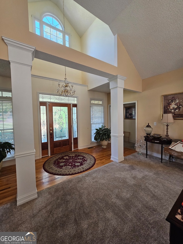 foyer with hardwood / wood-style flooring, high vaulted ceiling, decorative columns, and an inviting chandelier