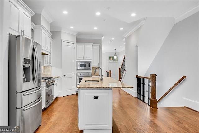 kitchen with light stone countertops, appliances with stainless steel finishes, light wood-type flooring, white cabinetry, and a kitchen island with sink