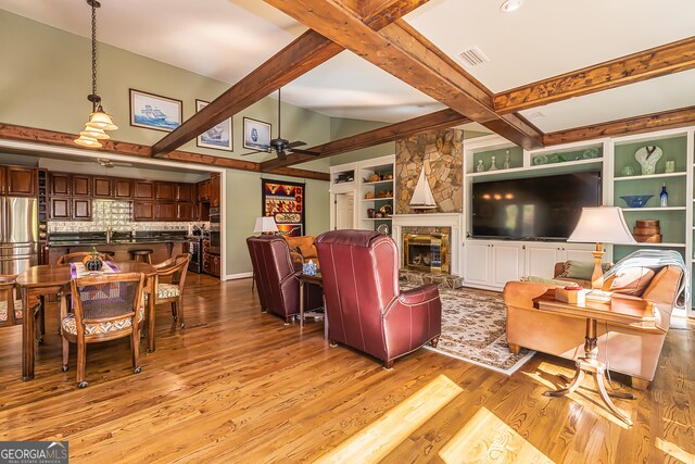 living room with a stone fireplace, beam ceiling, ceiling fan, and light hardwood / wood-style flooring