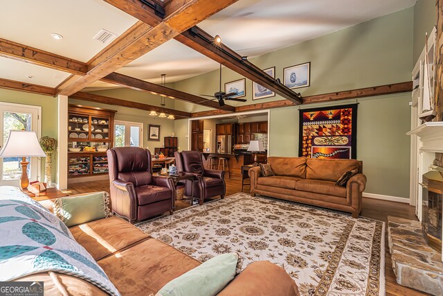 living room featuring a stone fireplace, wood-type flooring, ceiling fan, and beam ceiling