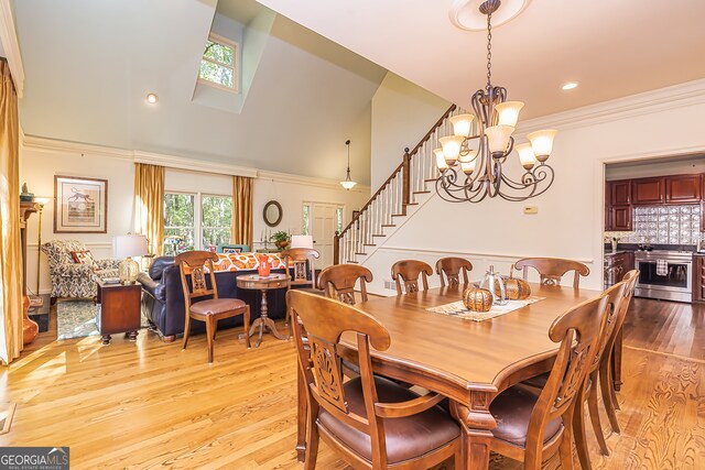 dining space featuring high vaulted ceiling, light wood-type flooring, a notable chandelier, and crown molding