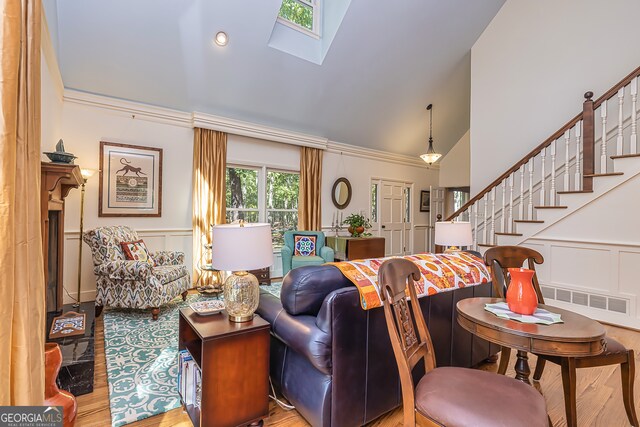 living room with crown molding, high vaulted ceiling, light hardwood / wood-style floors, and a skylight