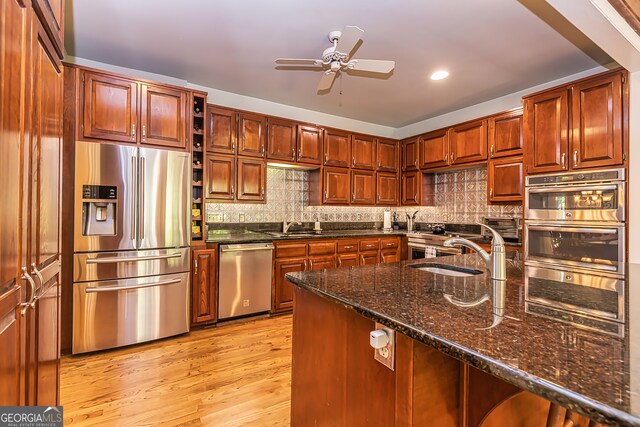 kitchen with stainless steel appliances, light hardwood / wood-style floors, dark stone counters, sink, and backsplash