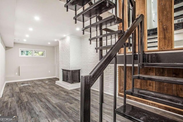 staircase featuring brick wall, a brick fireplace, and wood-type flooring