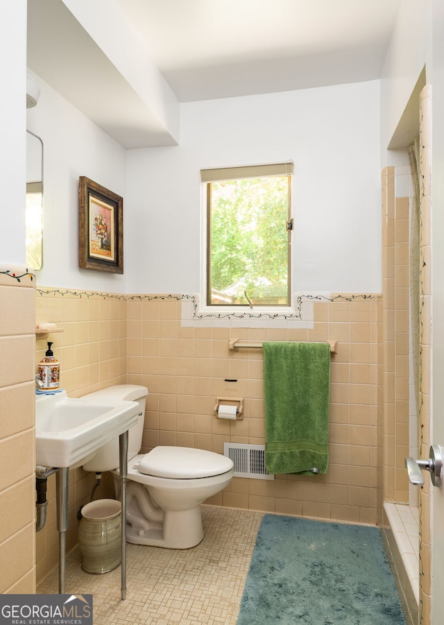 bathroom with toilet, a shower, tile walls, and tile patterned flooring