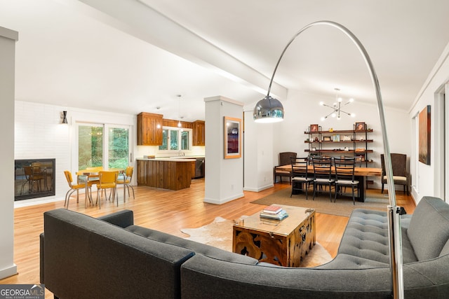 living room featuring a large fireplace, a chandelier, vaulted ceiling with beams, light hardwood / wood-style flooring, and sink