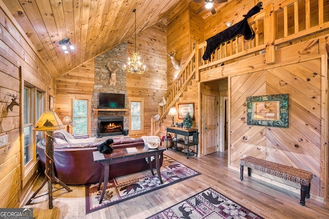 living room featuring hardwood / wood-style flooring, wooden walls, an inviting chandelier, a fireplace, and high vaulted ceiling