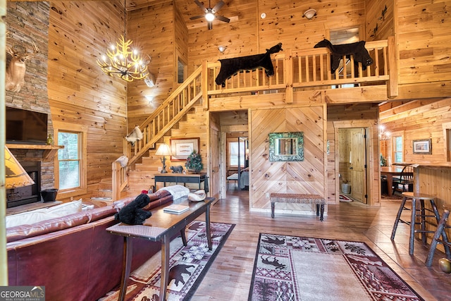 living room with a high ceiling, a stone fireplace, hardwood / wood-style flooring, wooden walls, and ceiling fan with notable chandelier