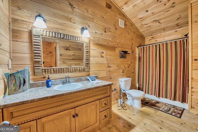 bathroom featuring lofted ceiling, hardwood / wood-style flooring, toilet, vanity, and wooden walls