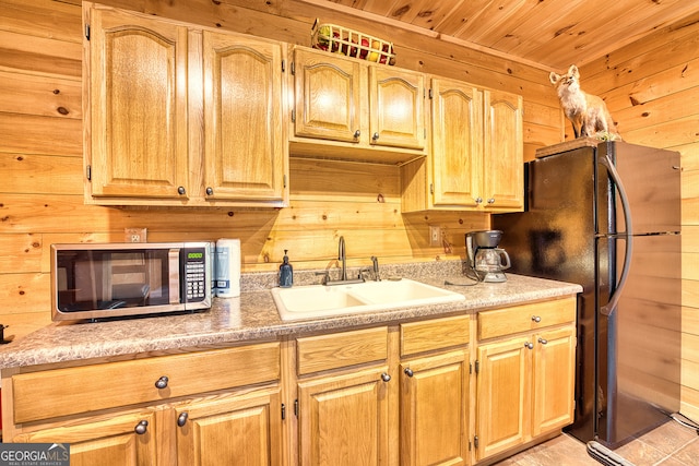 kitchen featuring black fridge, sink, wooden ceiling, and wood walls