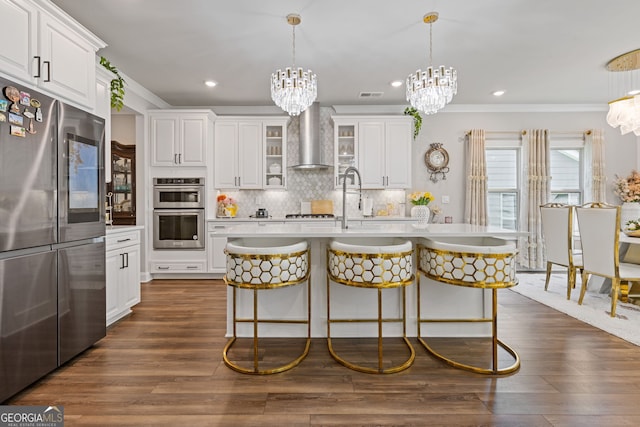 kitchen with wall chimney exhaust hood, dark wood-type flooring, a kitchen island with sink, and stainless steel appliances