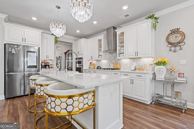 kitchen with appliances with stainless steel finishes, wall chimney exhaust hood, white cabinets, and a breakfast bar area