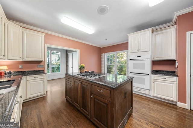 kitchen with dark hardwood / wood-style flooring, stainless steel gas stovetop, white double oven, and a wealth of natural light