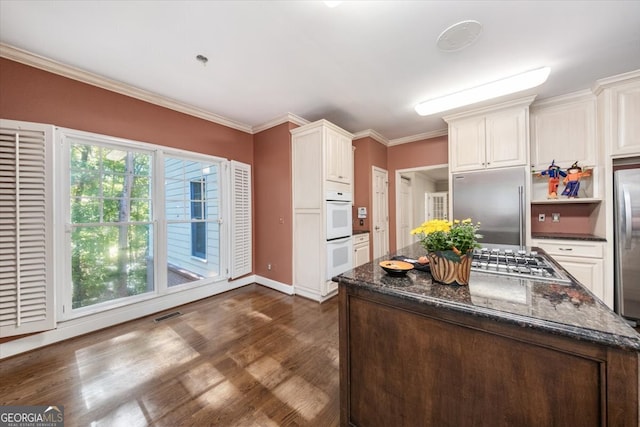 kitchen with white cabinetry, stainless steel appliances, dark stone counters, dark wood-type flooring, and ornamental molding