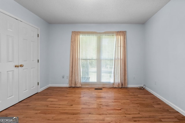 empty room featuring a textured ceiling, light wood-type flooring, and a wealth of natural light