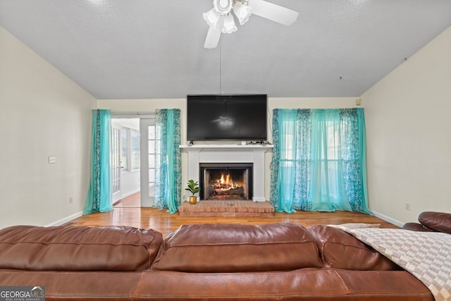 living room with lofted ceiling, wood-type flooring, a brick fireplace, a textured ceiling, and ceiling fan