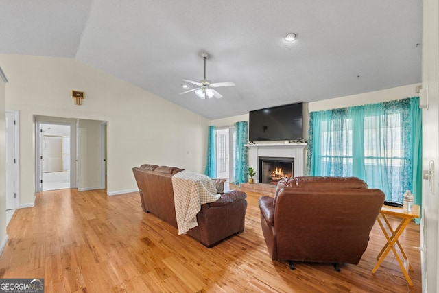 living room with a brick fireplace, ceiling fan, light wood-type flooring, and vaulted ceiling