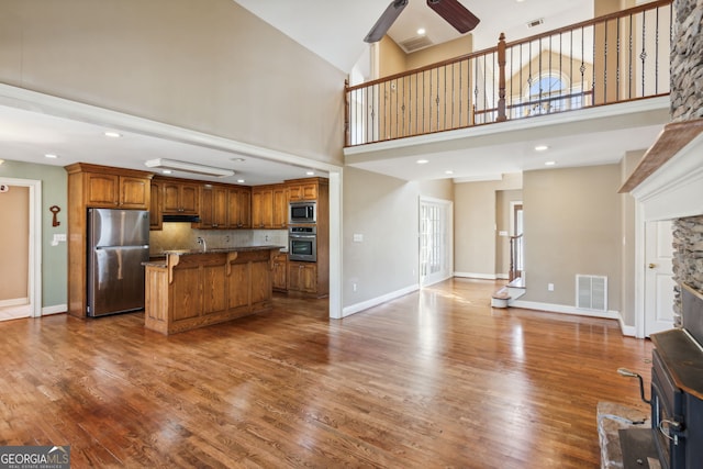 kitchen featuring hardwood / wood-style floors, ceiling fan, high vaulted ceiling, stainless steel appliances, and a center island