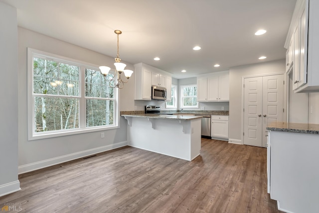 kitchen featuring kitchen peninsula, appliances with stainless steel finishes, decorative light fixtures, hardwood / wood-style flooring, and white cabinets