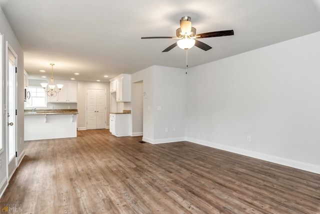 unfurnished living room with ceiling fan with notable chandelier and hardwood / wood-style flooring