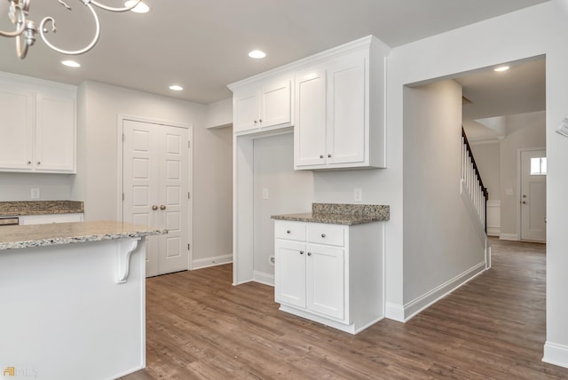 kitchen featuring dark wood-type flooring, an inviting chandelier, light stone counters, white cabinetry, and a breakfast bar area