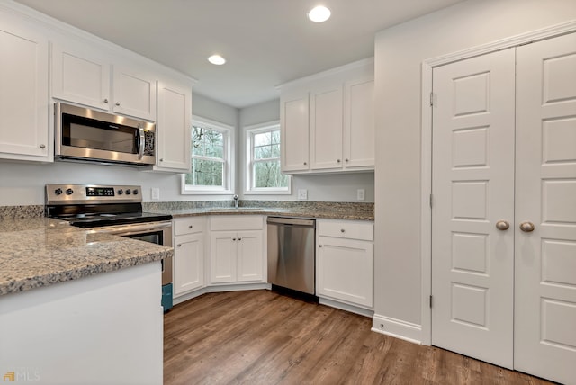 kitchen with white cabinetry, sink, light stone counters, appliances with stainless steel finishes, and light wood-type flooring