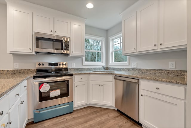 kitchen with light stone countertops, appliances with stainless steel finishes, sink, white cabinets, and light hardwood / wood-style floors