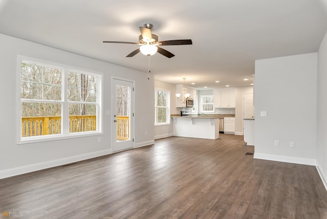 unfurnished living room with ceiling fan with notable chandelier and dark hardwood / wood-style flooring